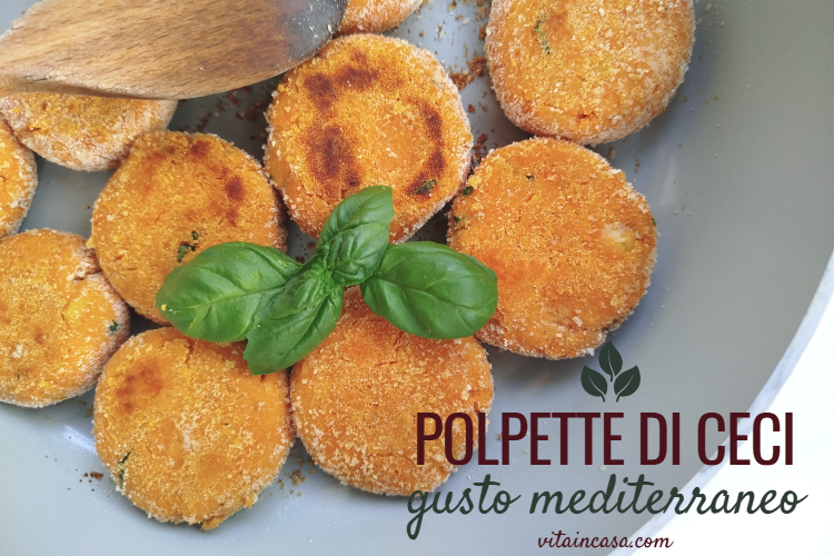 Veduta dall'alto di polpette di ceci dorate in una padella grigia, con un cucchiaio di legno e foglie di basilico fresco. Nell'angolo in basso a sinistra è presente la scritta "polpette di ceci - gusto mediterraneo by vitaincasa.com".